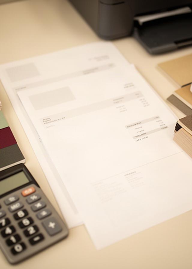 Invoice and printed order sheet arranged beside a calculator and paper samples in a small print office